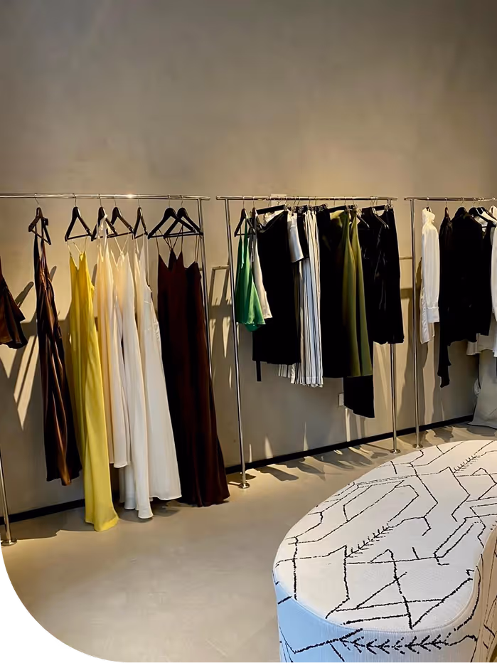 Clothing rack with dresses, skirts, and tops in various colors in a room with a patterned bench.
