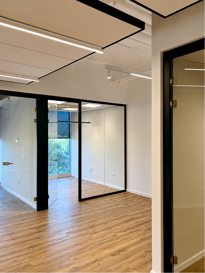 Modern empty office space with wood flooring, glass walls, and ceiling light panels.