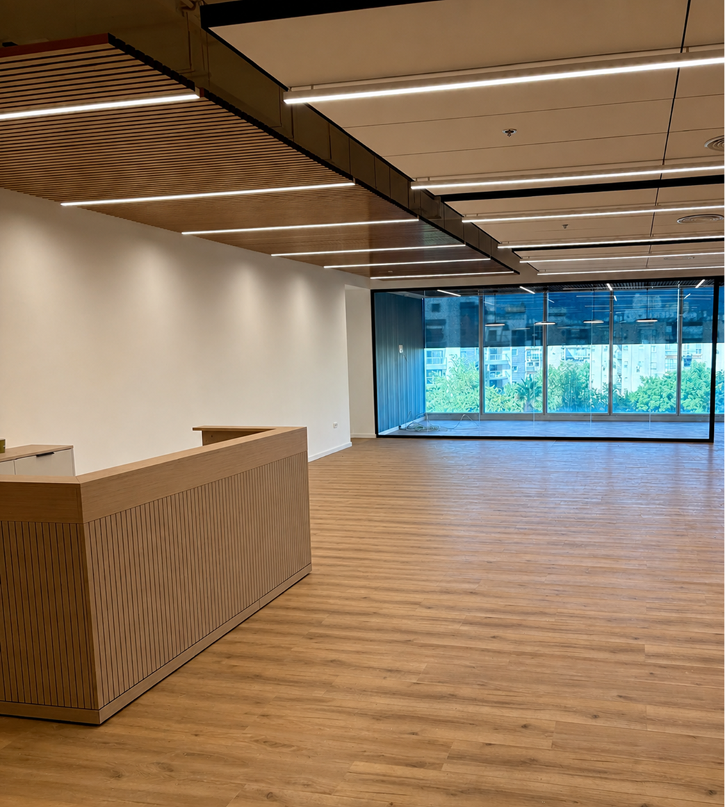 Modern empty office with wooden floor, a reception desk, ceiling lights, and large glass windows showing city view.
