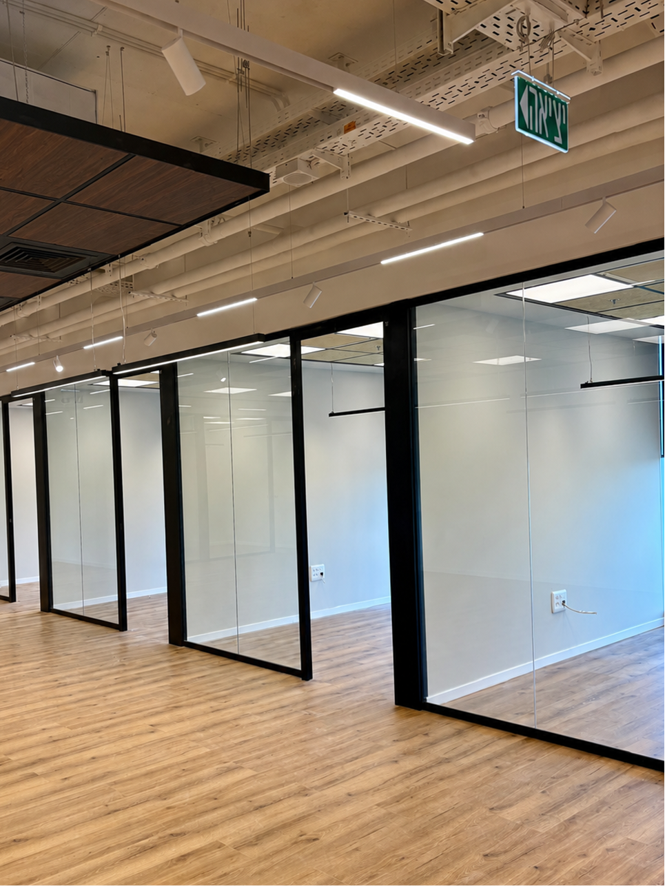 Empty modern office space with wooden floors and glass-walled rooms with black frames.