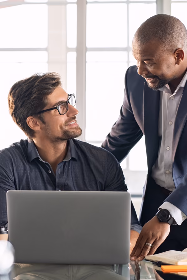 Two professional men smiling and talking over a laptop in an office