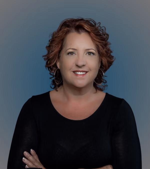 Smiling woman with curly brown hair wearing hoop earrings and a black top with arms crossed.