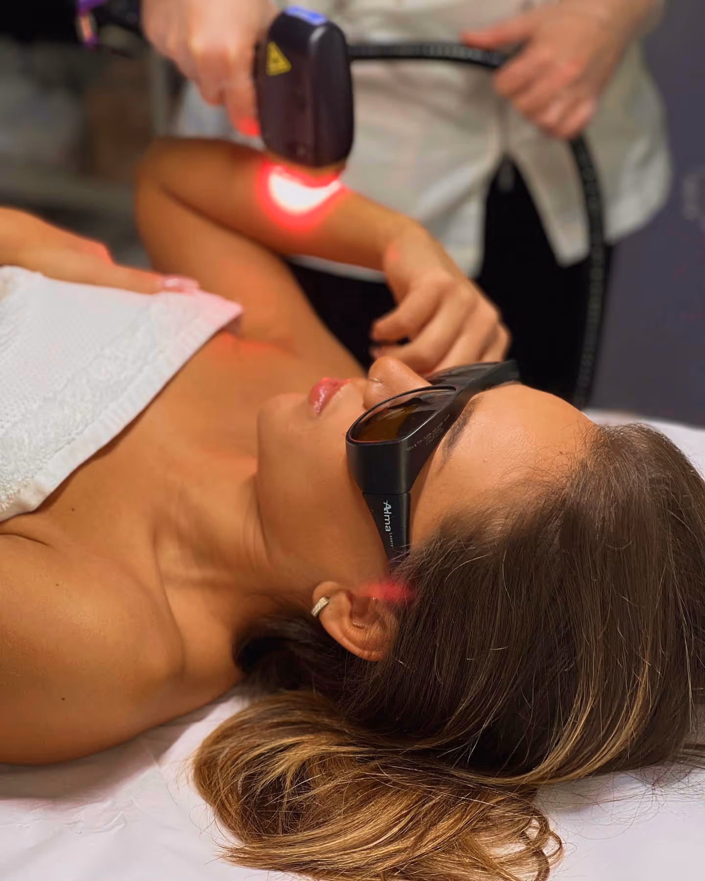 Woman wearing protective glasses receives laser light treatment on her arm in a clinic.