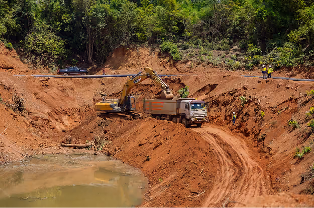 Excavatrice chargeant de la terre dans un camion sur un chantier de terrassement près d'un point d'eau.