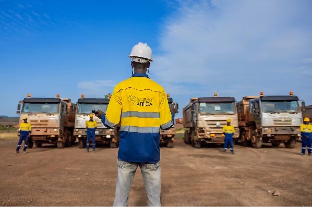 Un homme en équipement de sécurité supervise des ouvriers devant des camionsdans un chantier.