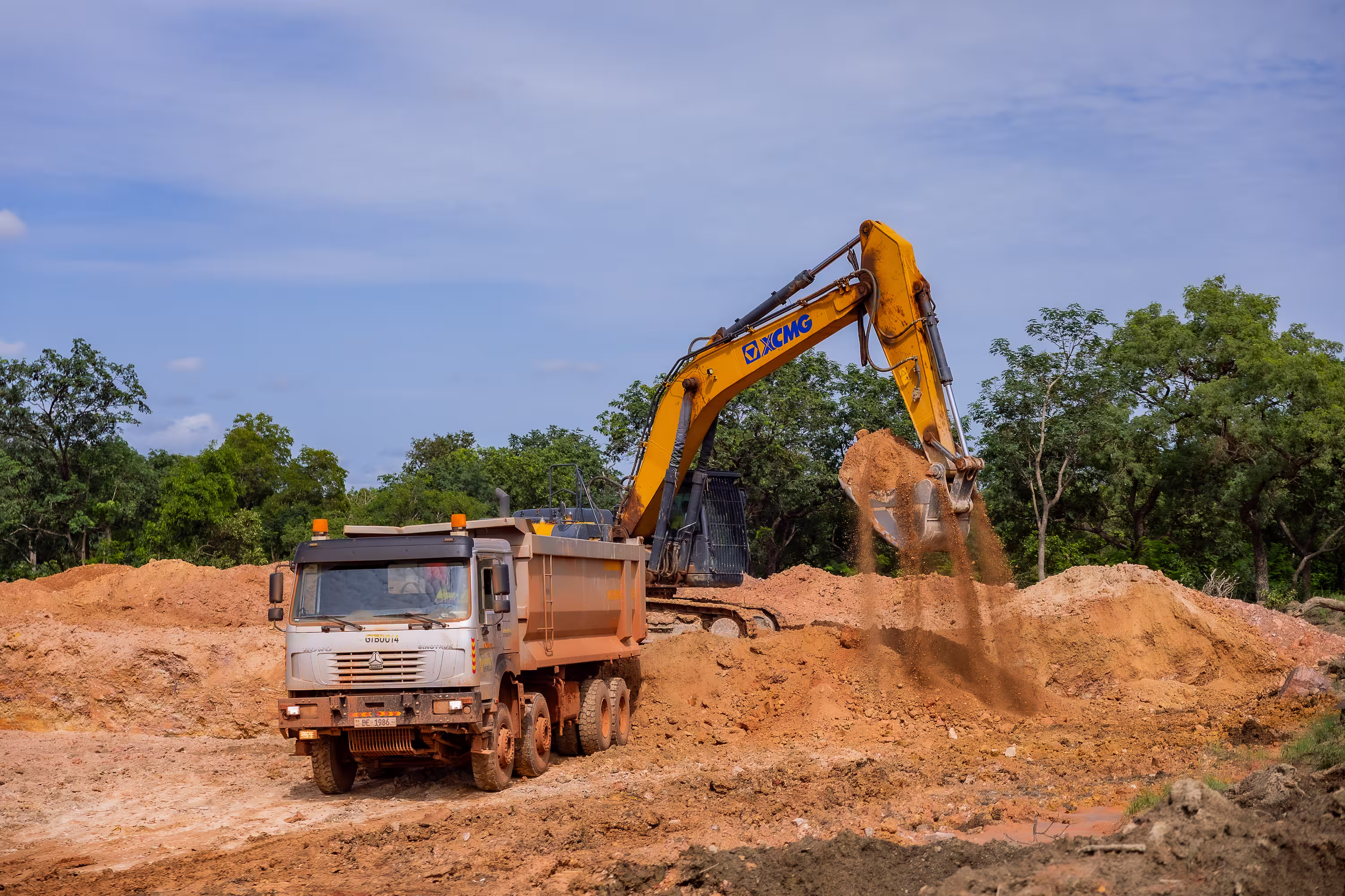 Une pelleteuse jaune décharge de la terre dans un camion benne sur un chantier.