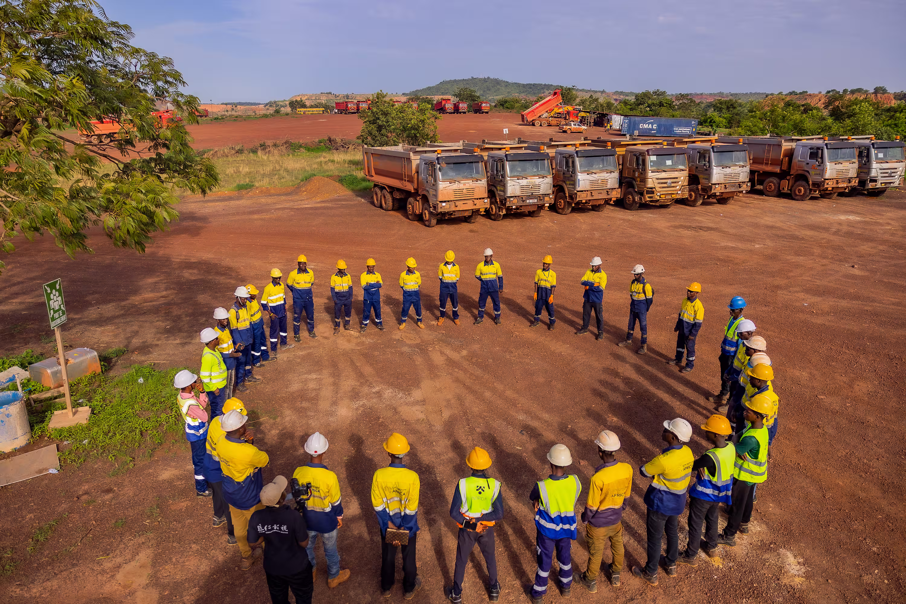 Travailleurs en tenue de chantier formant un cercle sur un terrain avec camions à l'arrière.