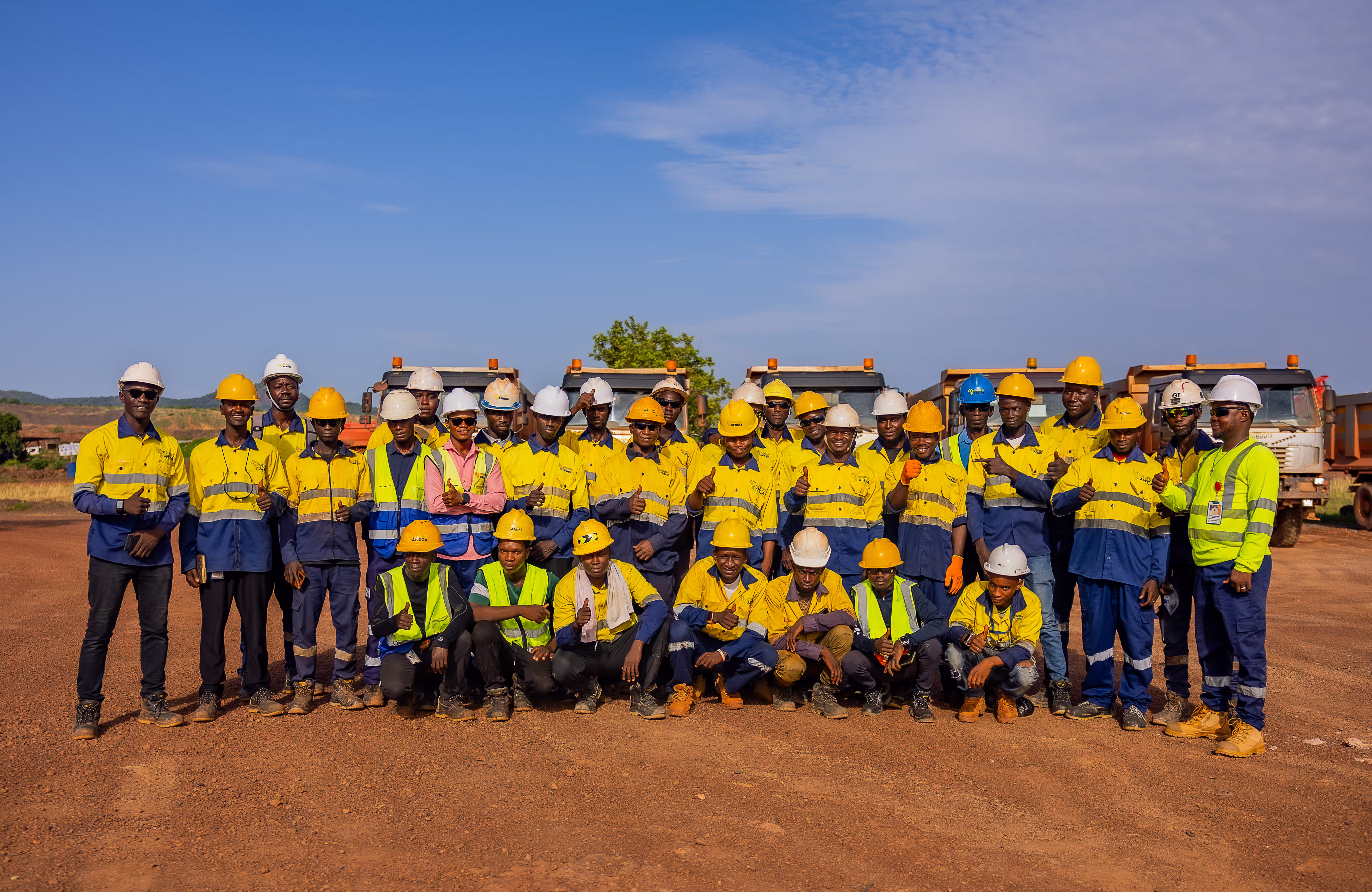 Groupe de travailleurs en tenue de sécurité jaune posant devant des camions sur un chantier.
