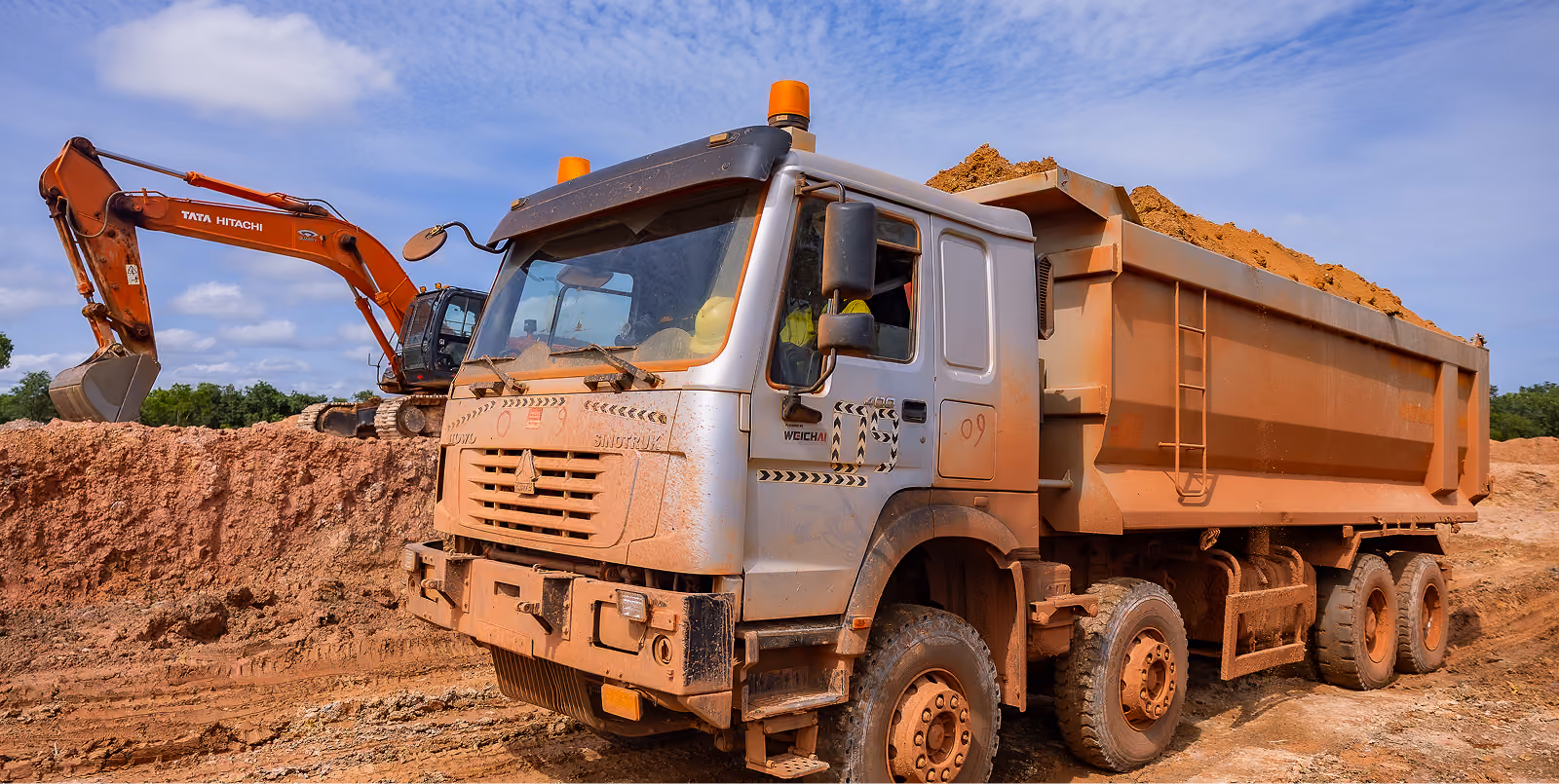 Camion benne chargé de terre à côté d'une pelleteuse sur un chantier de construction.