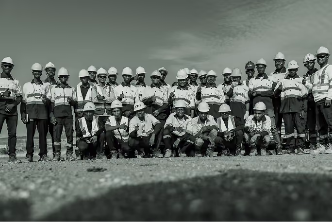 Groupe de travailleurs en tenue de chantier et casque, posant dehors devant un ciel nuageux.