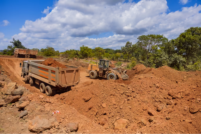 Camions et bulldozer en train de déplacer de la terre sur un chantier sous ciel nuageux.
