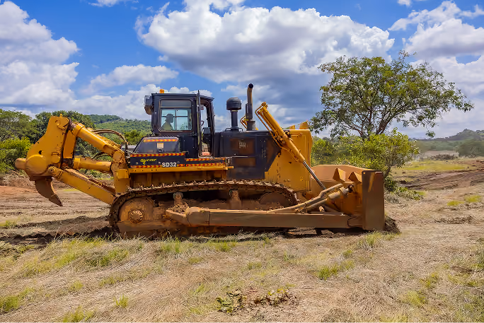 Un bulldozer jaune stationné sur un terrain herbeux sous un ciel bleu avec des nuages blancs.