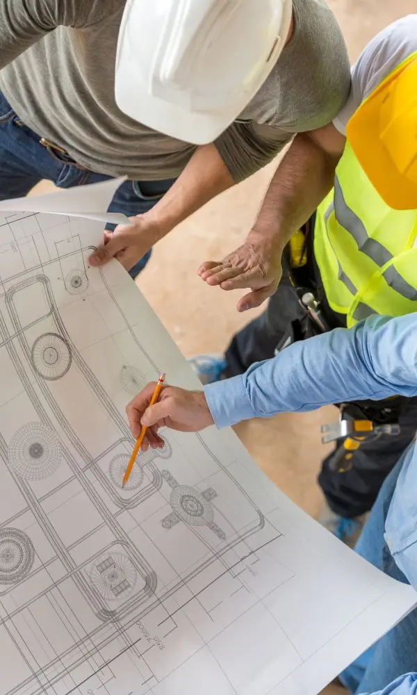 Construction professionals reviewing technical drawings and discussing project details on site while wearing safety equipment.