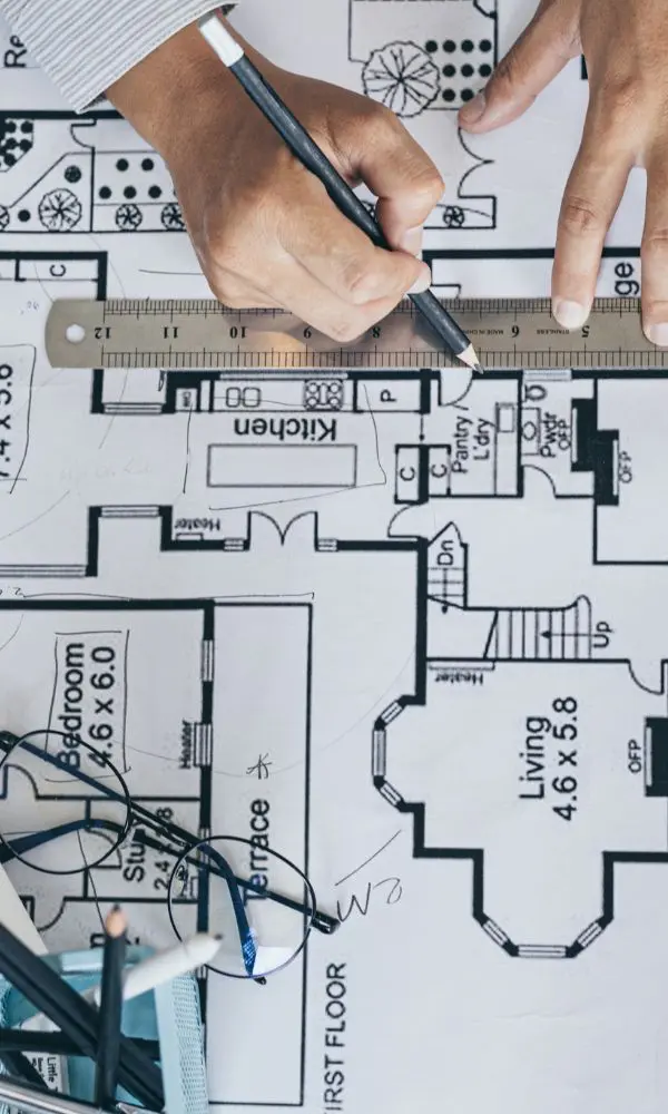 Close up of an engineer reviewing and marking architectural floor plan drawings with measurement tools and technical notes.