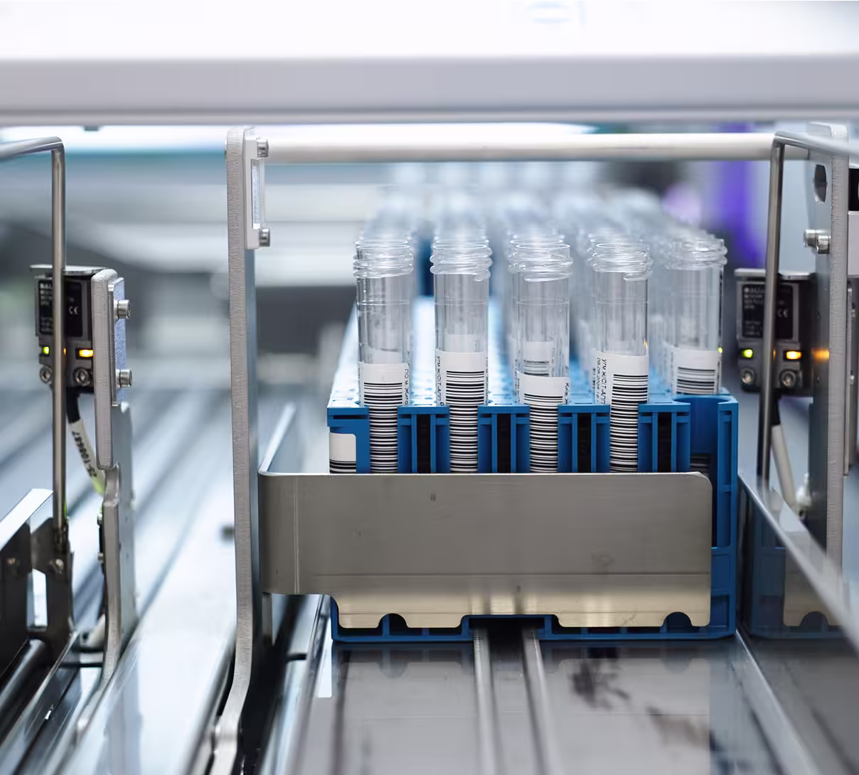 Rows of clear test tubes with barcode labels in a blue rack within a laboratory machine.