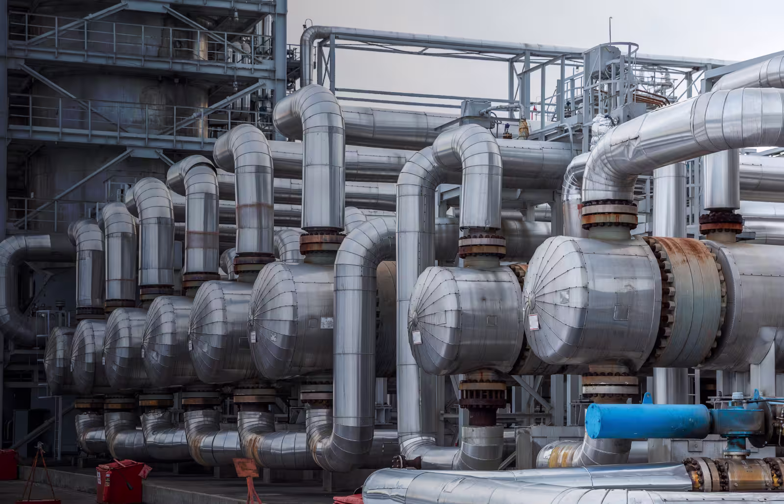 Rows of large silver industrial pipes and valves in a factory or energy plant.