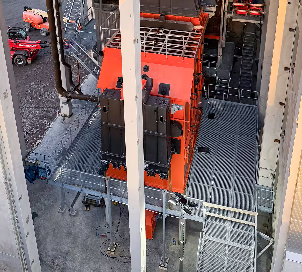 Large orange industrial boiler system inside a utility facility with metal catwalks and pipes.