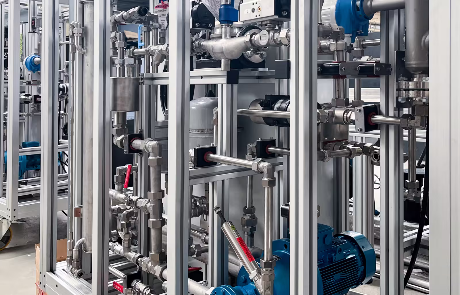 Complex industrial conditioning unit with metal pipes, valves, and a blue motor in a factory setting.