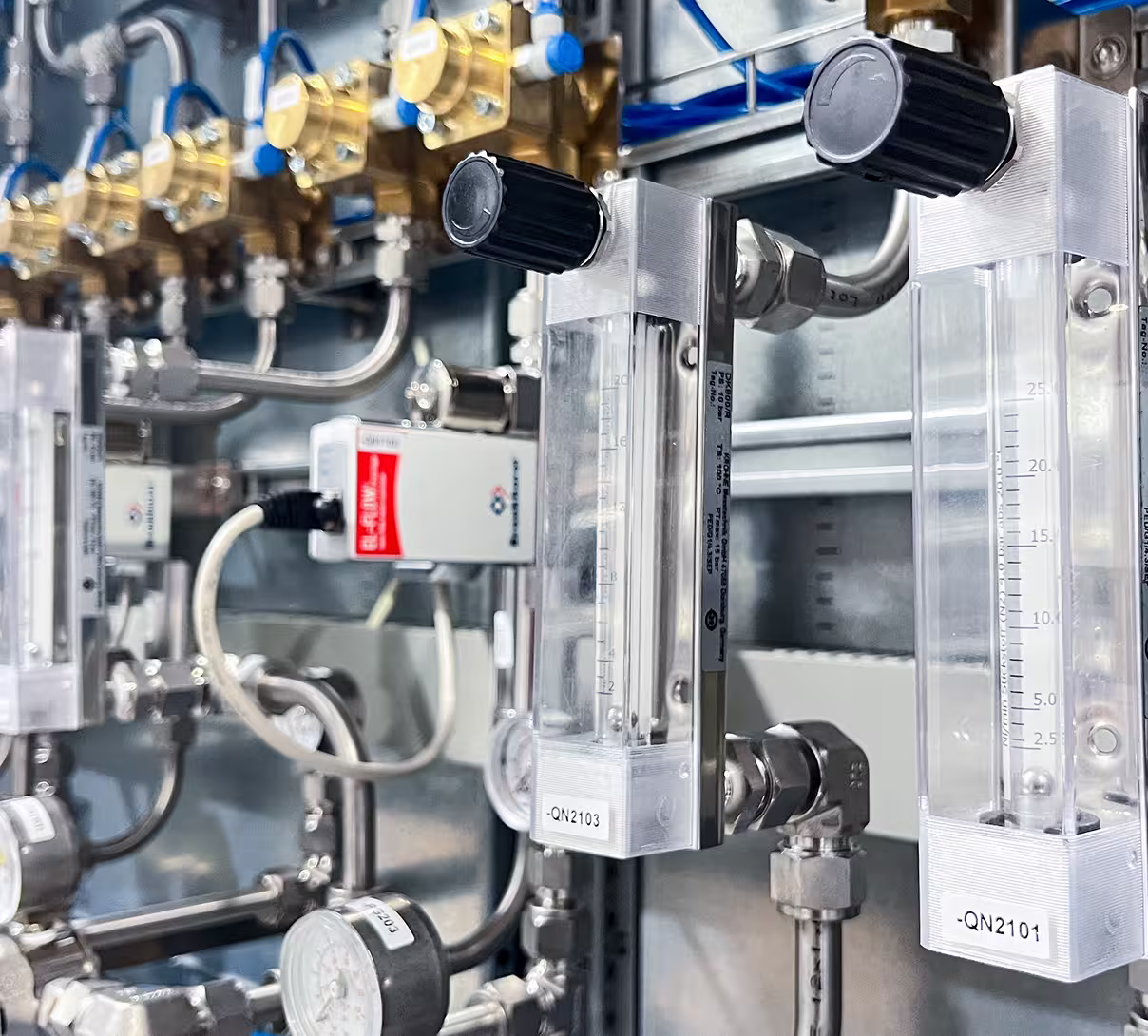 Close-up of industrial flow meters and pressure gauges with metal piping in a processing setup.