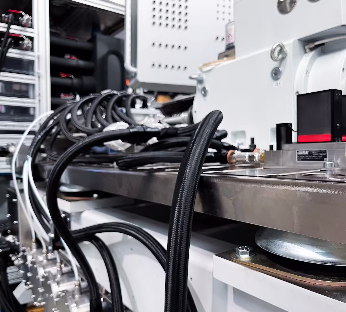 Close-up of black tubes connected to a metal industrial test bench in a factory setting.