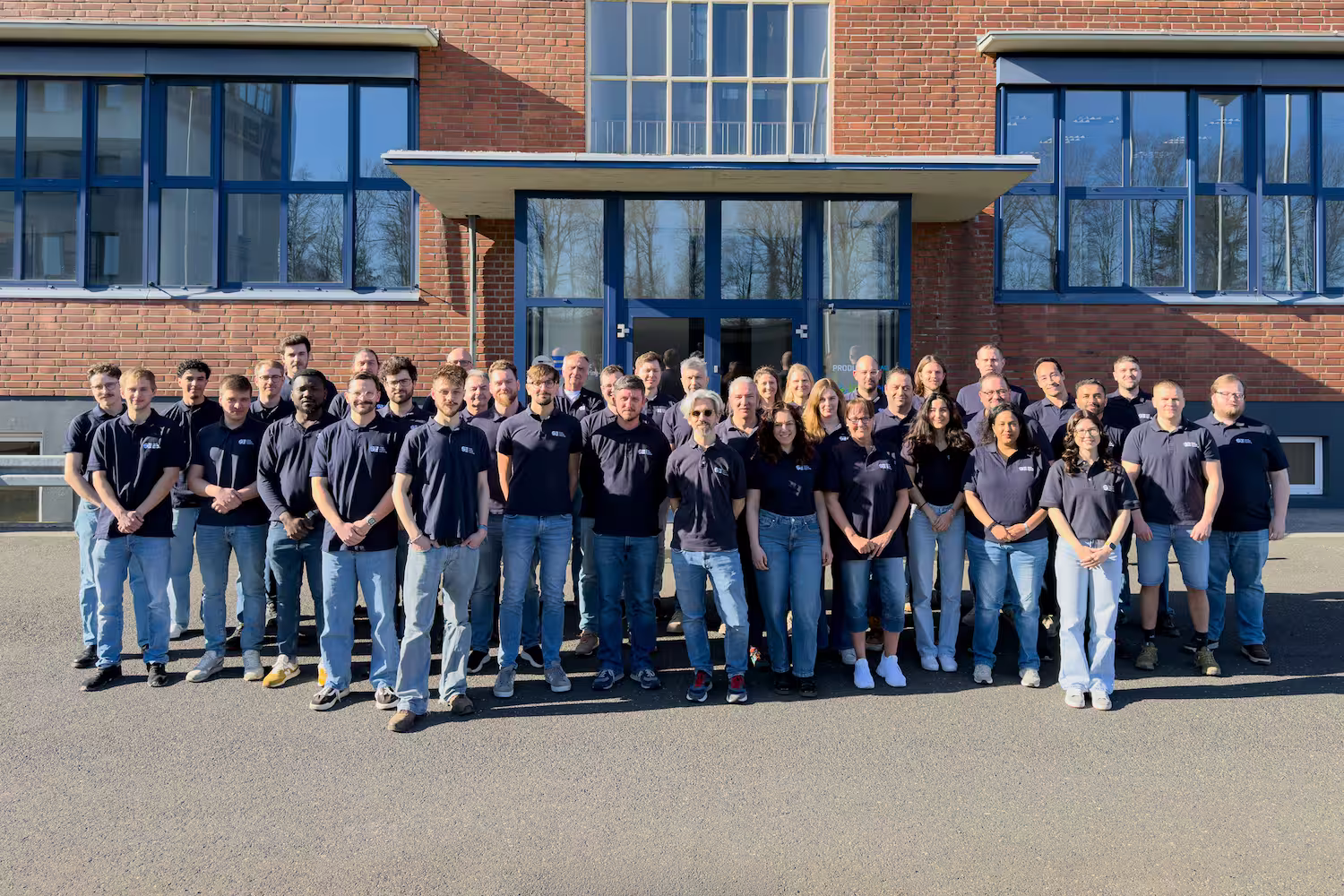 EUtech team wearing matching dark blue shirts standing outside a brick building on a sunny day.