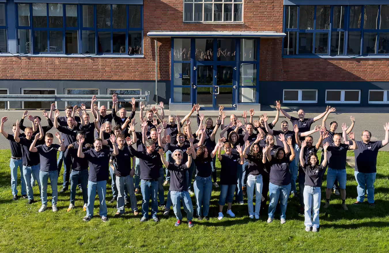 Das EUtech-Team steht auf einer Rasenfläche vor einem Gebäude und winkt mit beiden erhobenen Händen.