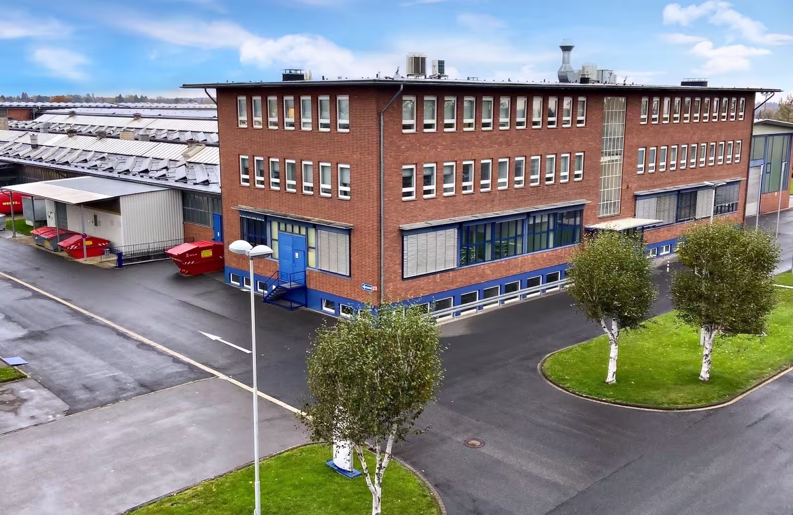 EUtech company building on site with brick façade, large windows, blue doors, and landscaped surroundings.