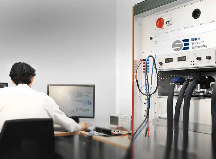 Engineer performing hardware-in-the-loop (HiL) testing at a computer connected to scientific engineering equipment.