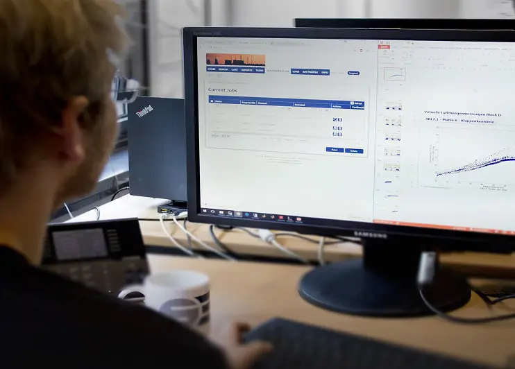 Data management specialist working at a dual-screen workstation displaying technical data and graphs.