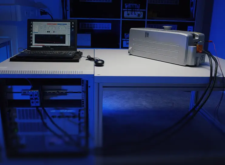 Laptop on white table rack test equipment connected to a battery for testing.