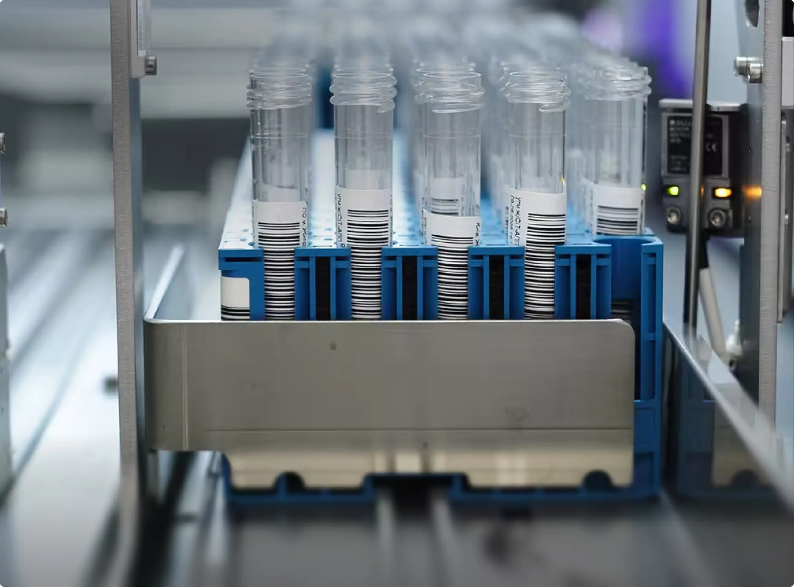 Rows of clear test tubes with barcode labels held in a blue rack inside lab equipment.
