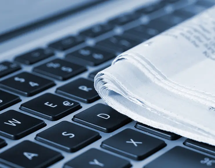 Rolled newspaper resting on a black computer keyboard.