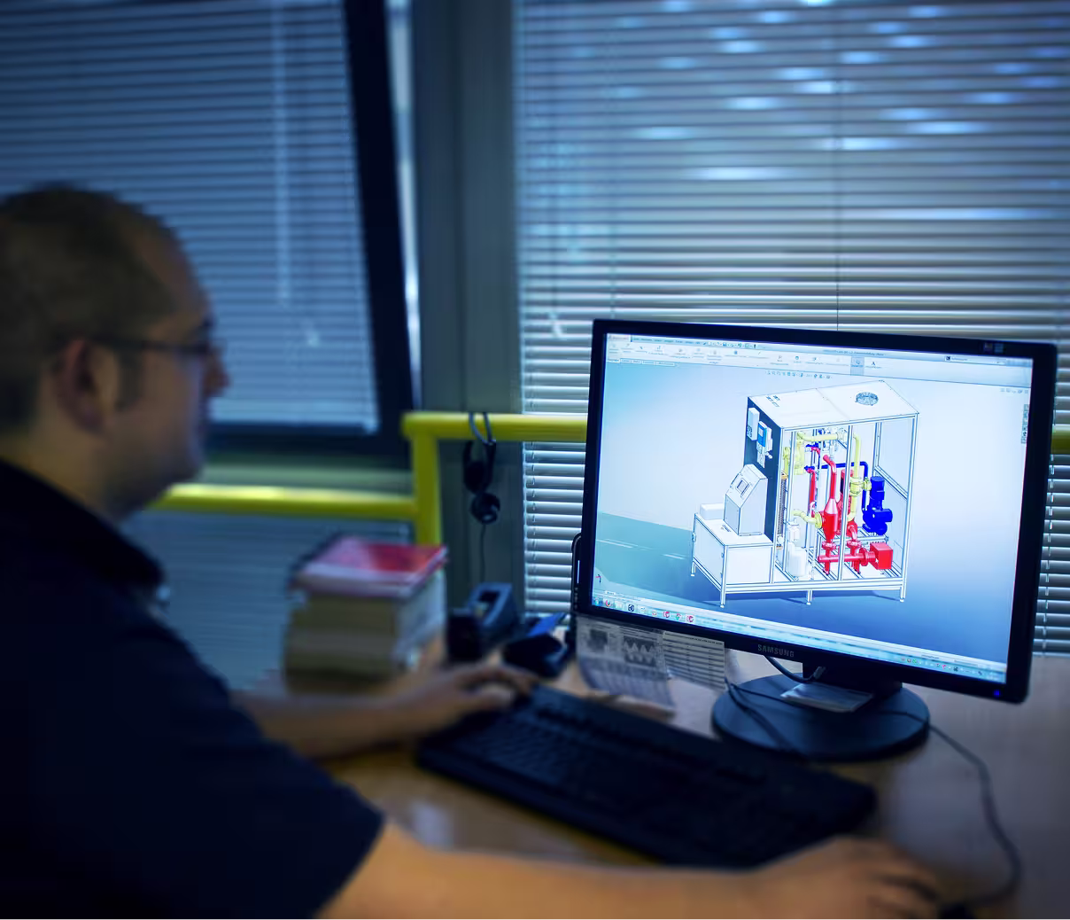 Person working on a computer with 3D mechanical design displayed on the monitor.