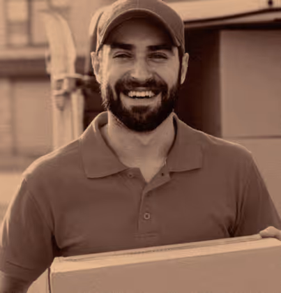 Man with a beard wearing a cap and polo shirt smiling while holding a cardboard box.