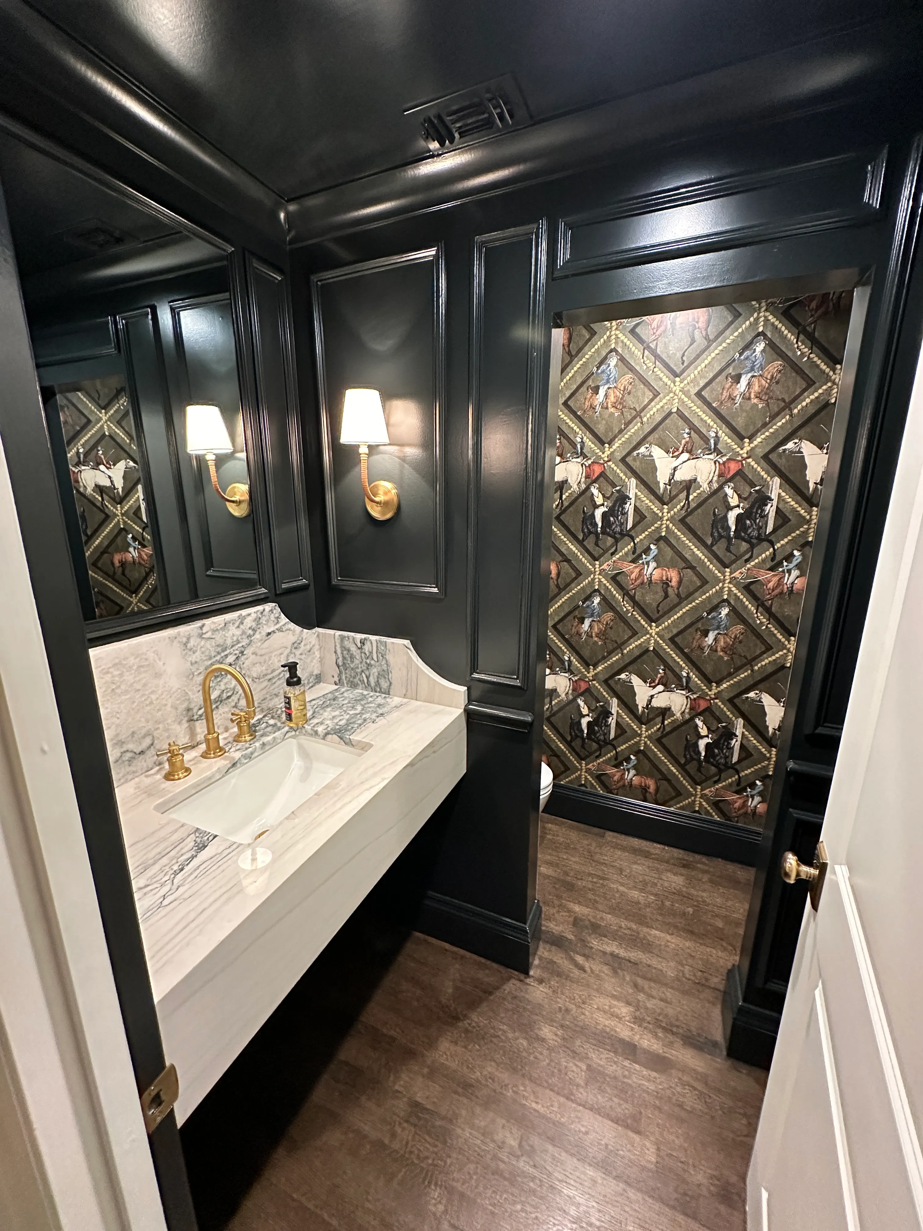 Black-paneled powder room with marble sink and brass faucet