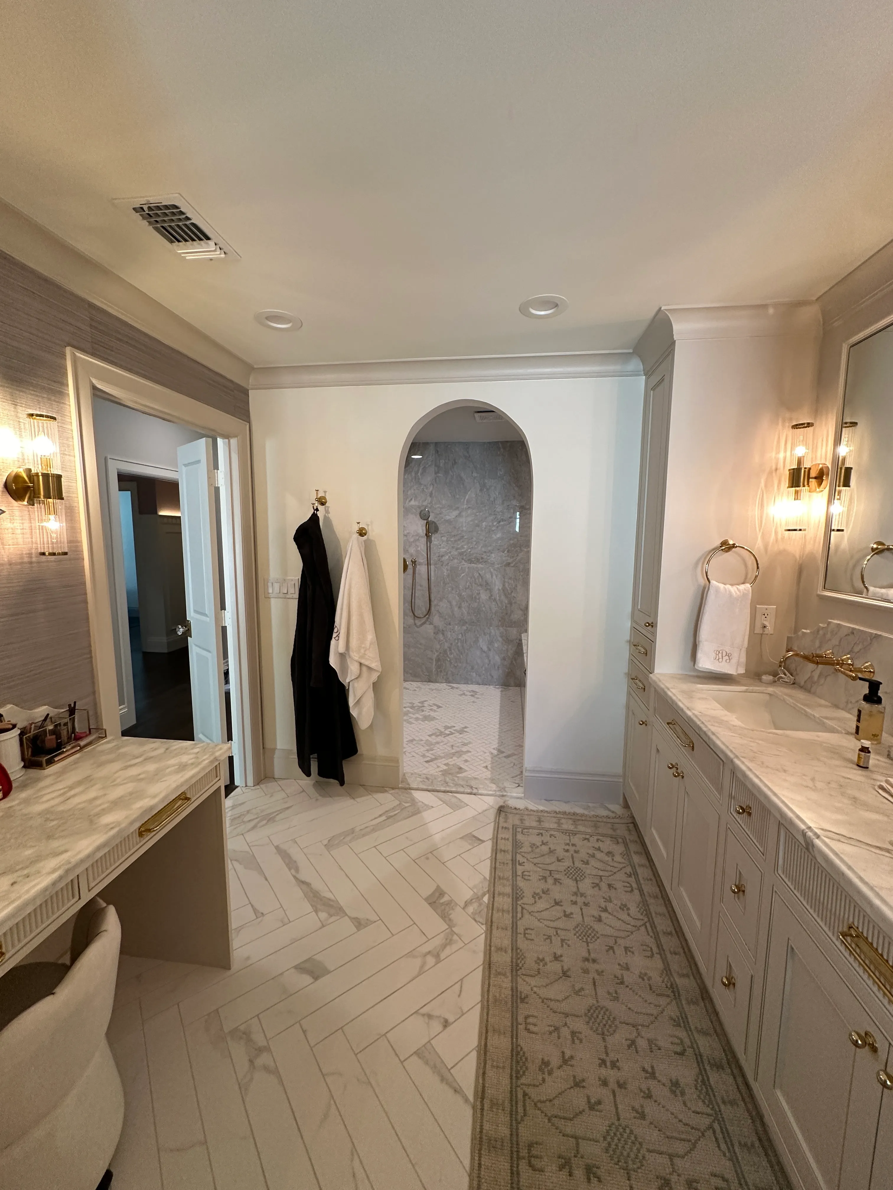 Primary bath with arched shower entry, herringbone floor and marble vanity