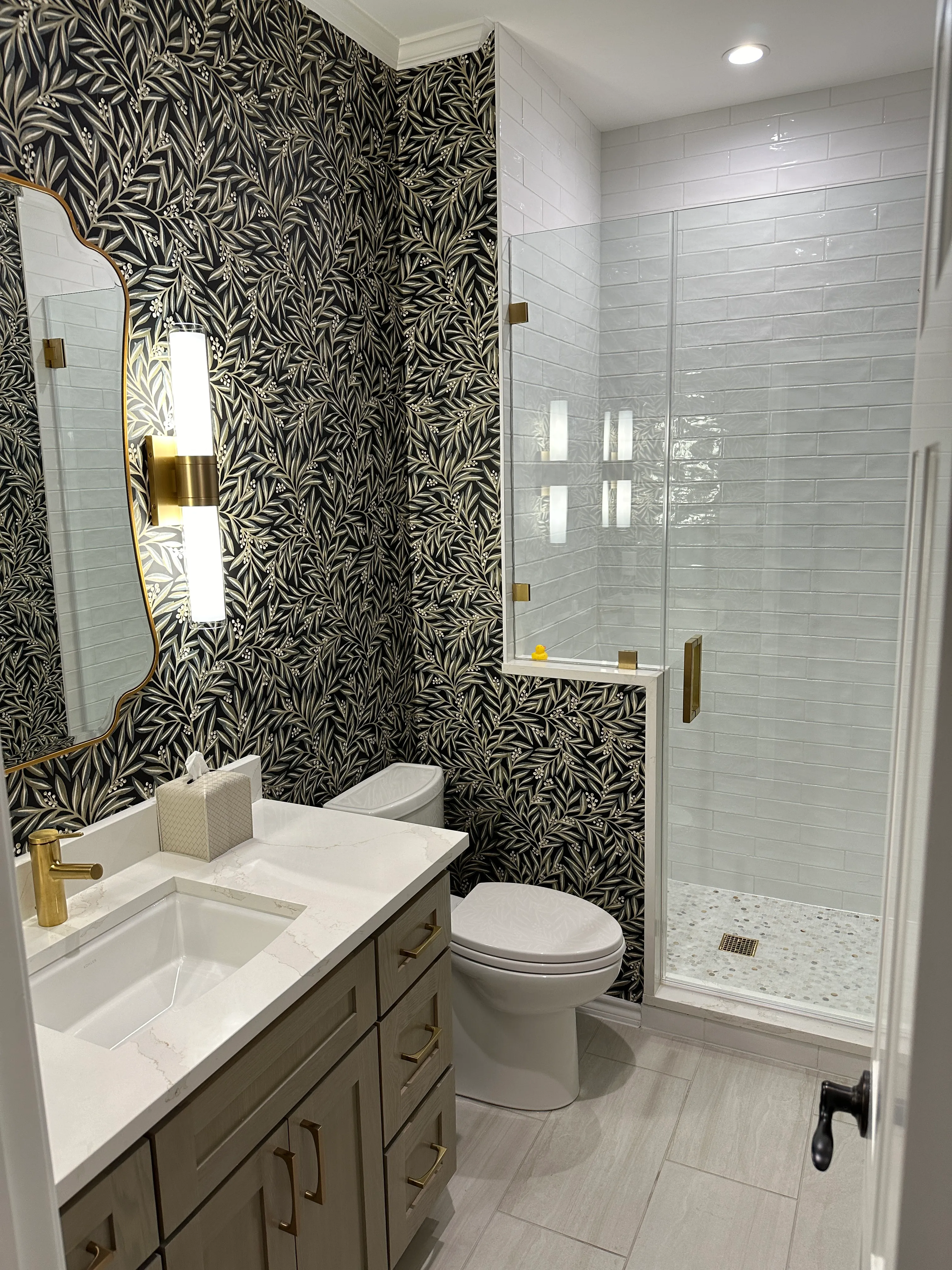 Bathroom with black leaf-pattern tile, glass shower and brass fixtures