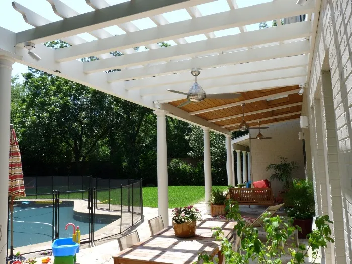 White pergola with wood ceiling fans over a patio dining area