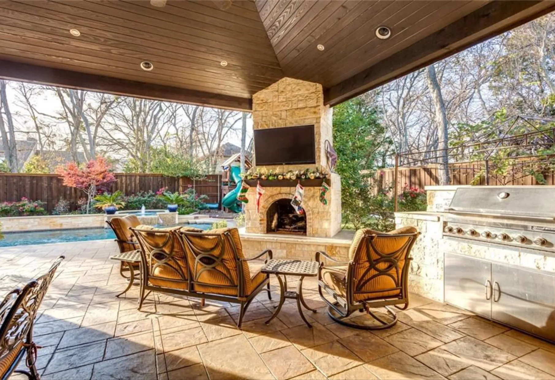 Covered outdoor living room with stone fireplace, TV and grill