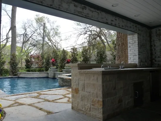 Outdoor kitchen with stone counter beside a flagstone pool deck