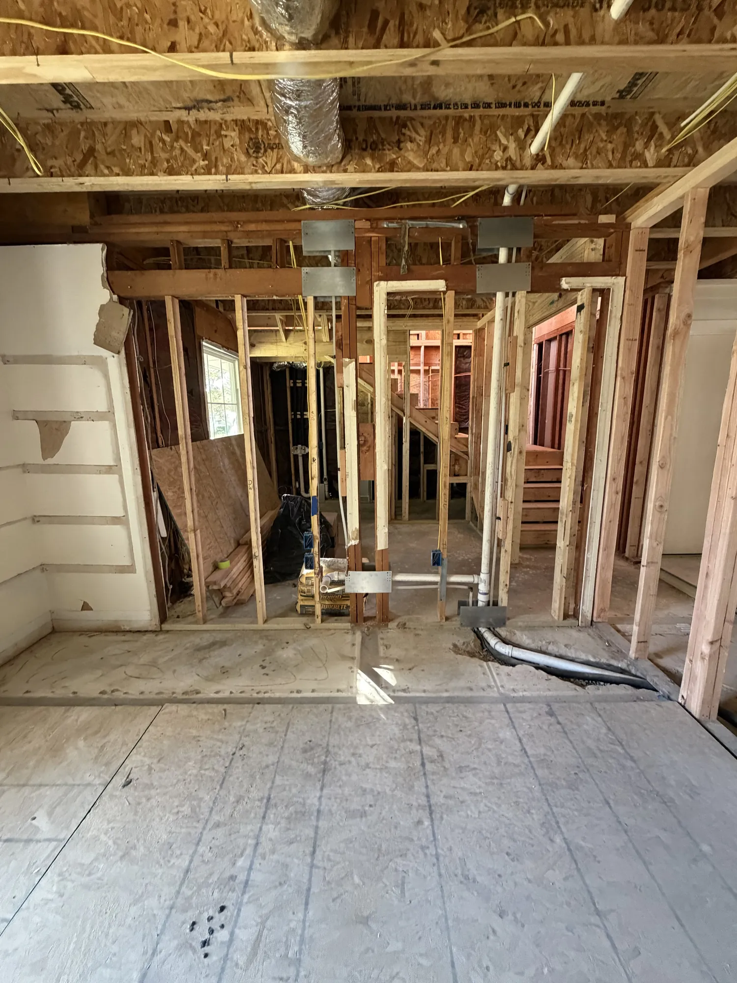 First-floor framing with plumbing drains, electrical wiring and ductwork overhead during rough-in