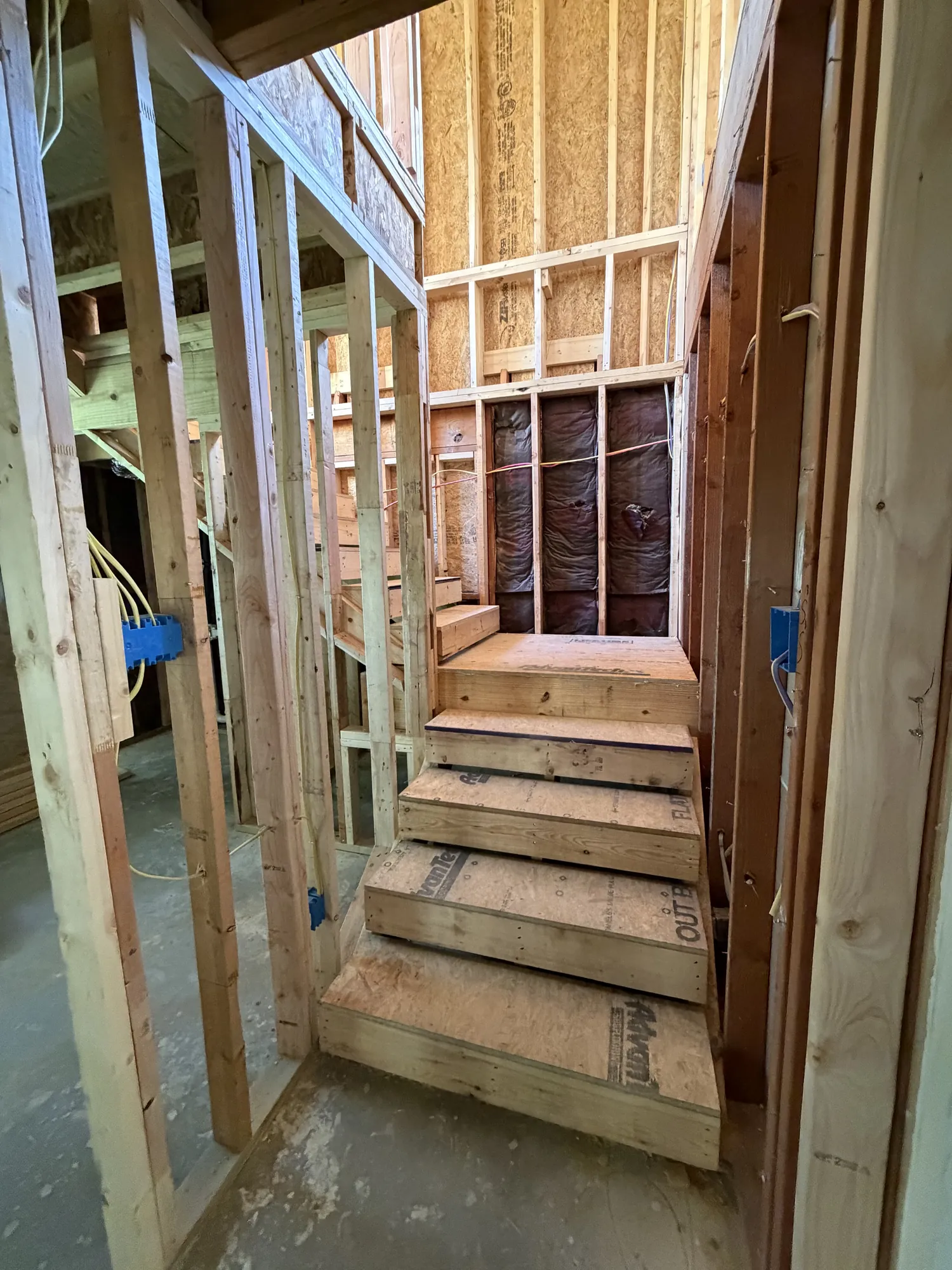 New staircase framed between floors with a landing and electrical boxes set in the walls