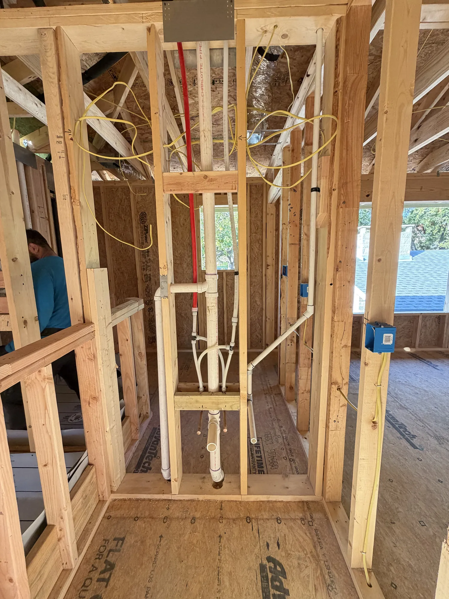 Plumbing rough-in with drain lines and red and white supply lines in a second-floor wall