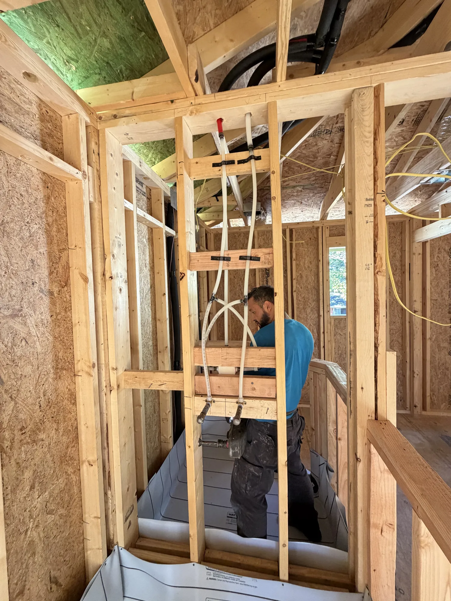 Plumber working on the shower valve rough-in above a framed shower pan
