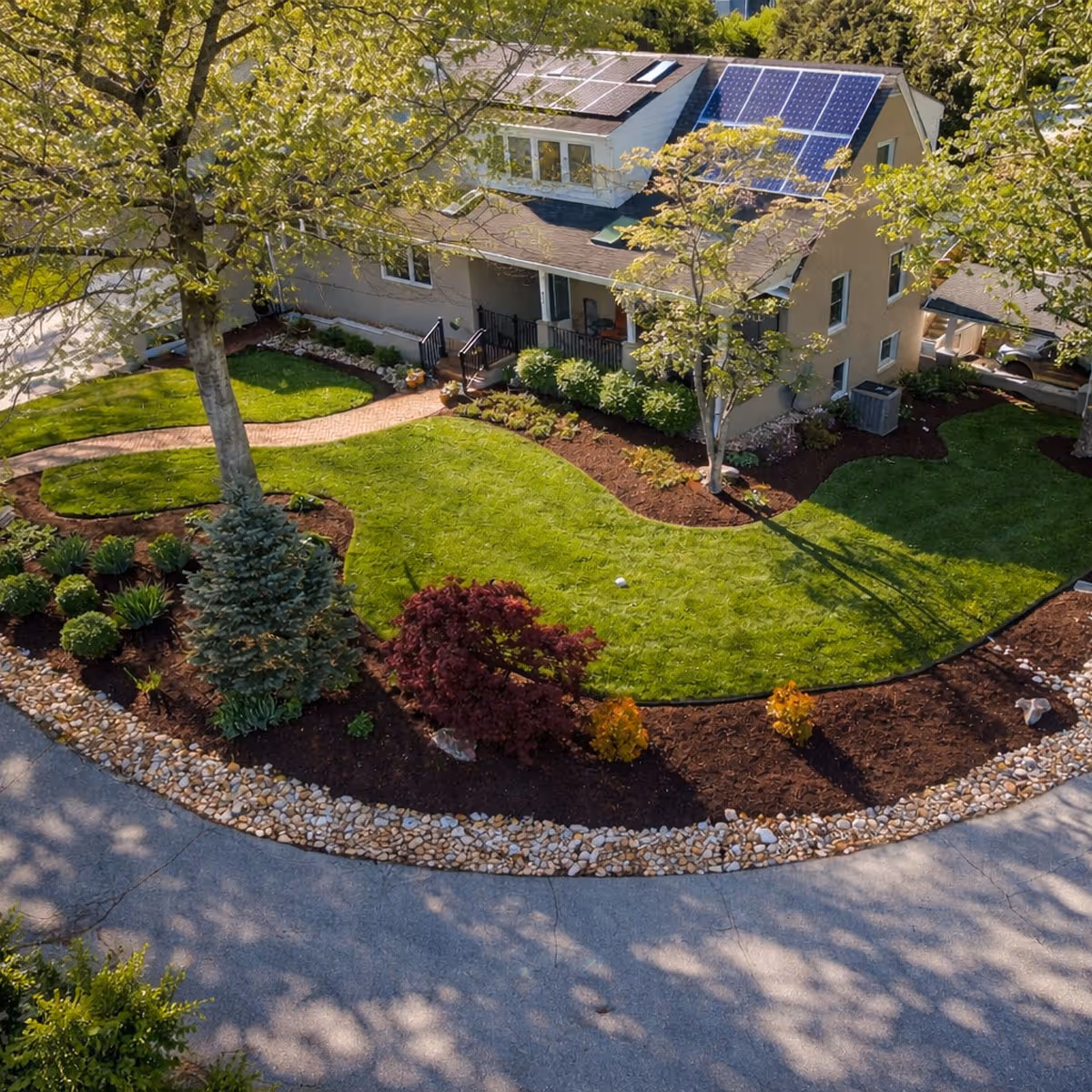 Aerial view of a professionally landscaped front yard featuring curved mulch beds, ornamental shrubs, a Japanese maple, and a brick paver walkway leading to a two-story home in the New River Valley.