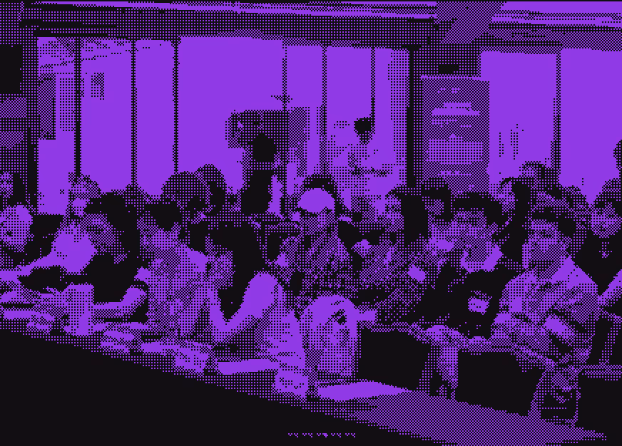 Group of people seated at long tables in a conference or seminar setting.