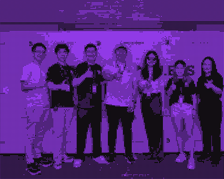 Seven people standing in a row, smiling and making thumbs-up gestures indoors.