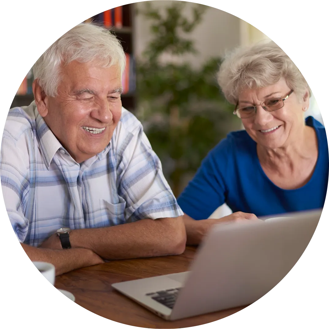 Smiling elderly man and woman looking at a laptop screen together at a wooden table.