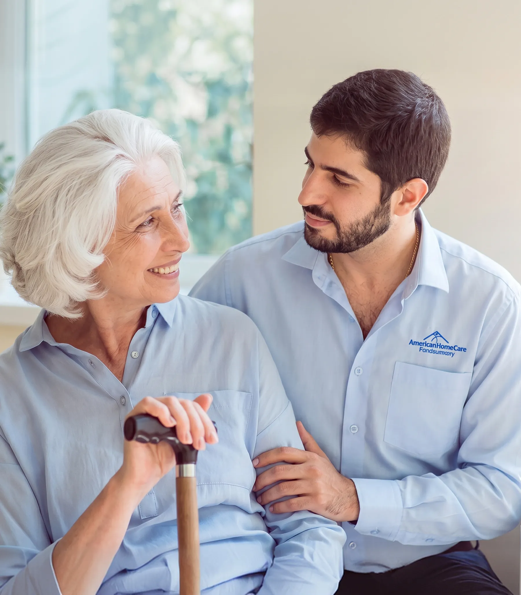 Smiling elderly woman with a cane looks at a man in a home care uniform holding her arm.