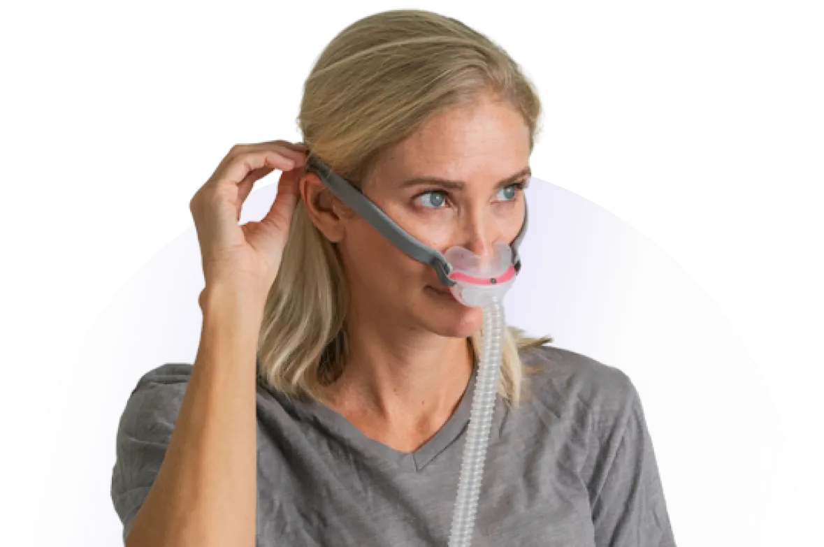 Blonde woman adjusting a gray CPAP mask worn on her face for sleep therapy.
